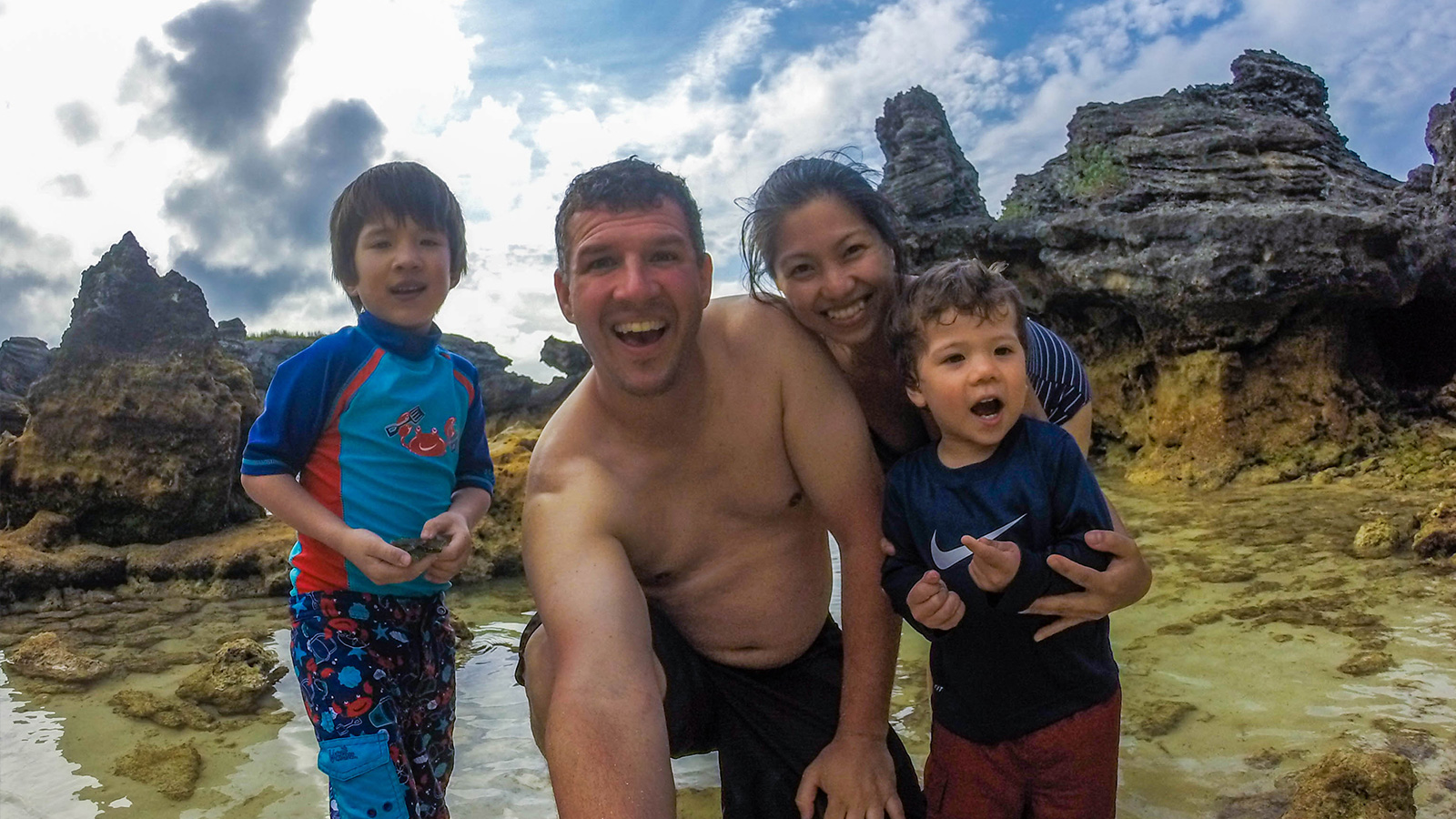 A young interracial family smiling on a beach. The family has two young boys, a Caucasian father and an Oriental mother