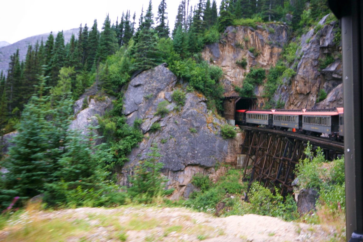 Whitepass and Yukon Railway train cars going into a tunnel in the Rocky Mountains.