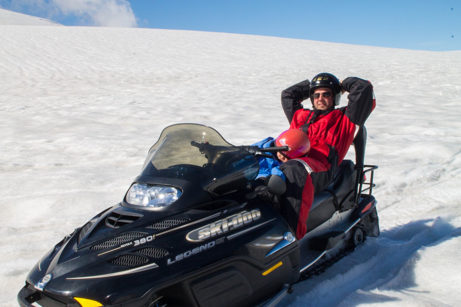Man sits on a snowmobile on an Icelandic Glacier with a sleeping child in his lap - helping kids find nap time on the road