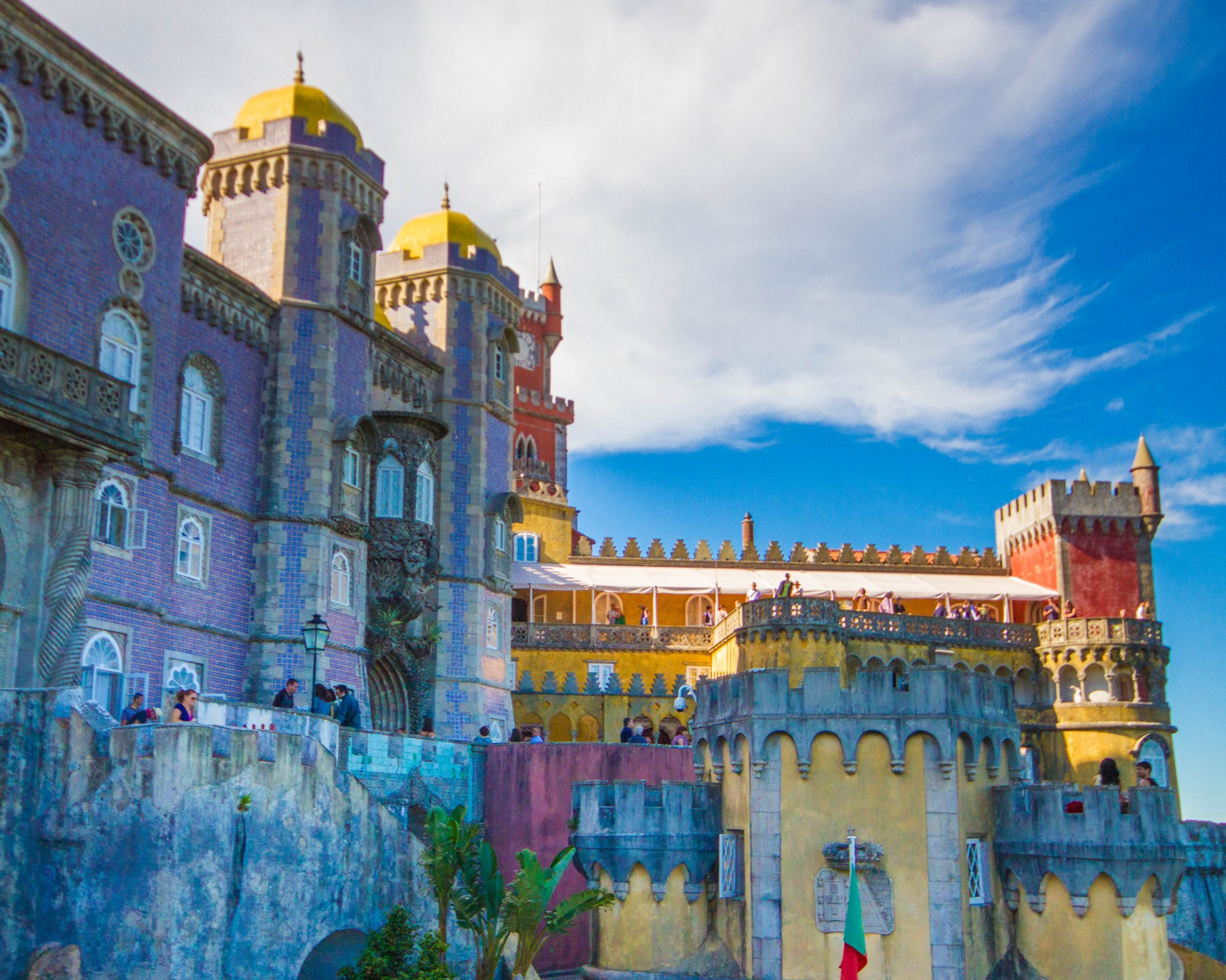 A castle with multi-coloured facade stands against a blue mountain sky - Sintra, Portugal