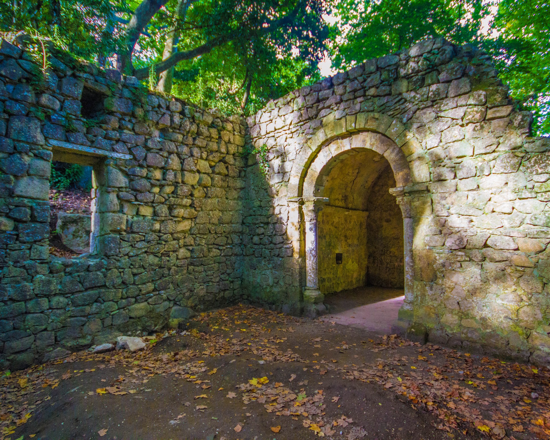 A ruined chapel sits in the woods and is lit up by sunlight through breaks in the trees - Sintra, Portugal