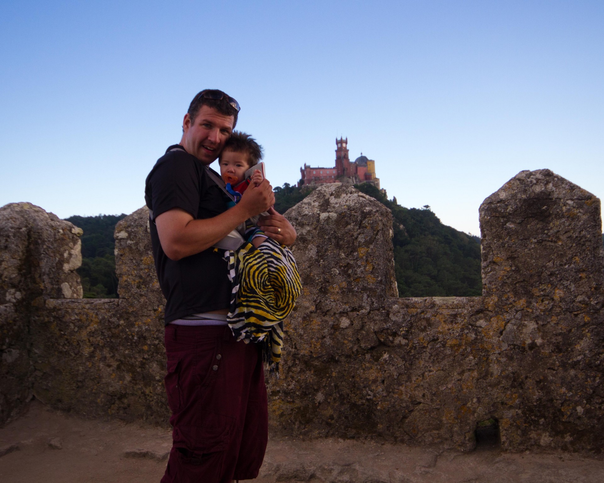 Father holds his son in a Baby Bjorn in front of Sintra Castle in Portugal - helping kids find nap time on the road