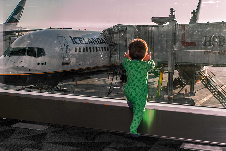 A toddler in pajamas looking out the window of an airport at an Icelandair plane at sunset as they prepare to travel Iceland's Golden Circle with kids