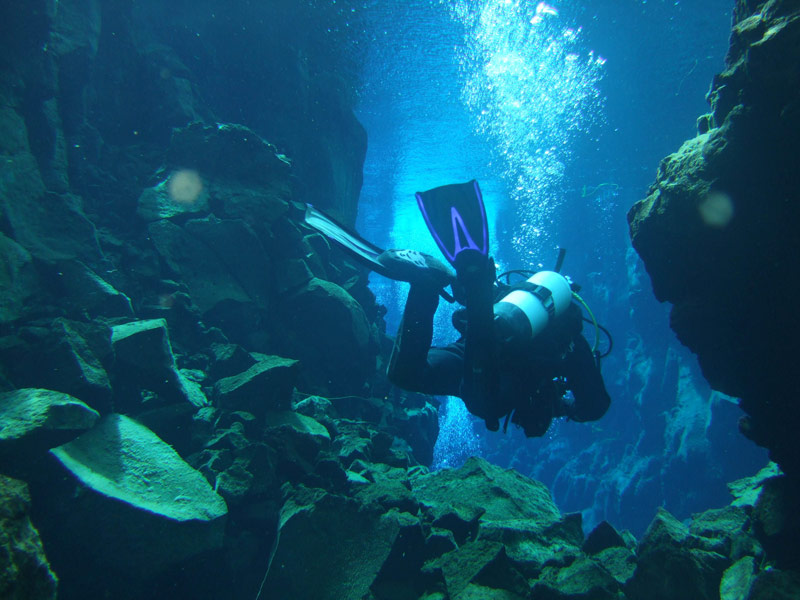 A SCUBA diver floats through narrow cracks in a fissure - Diving Iceland's Silfra