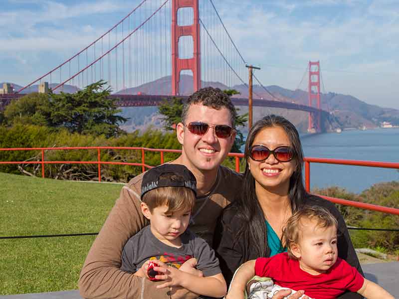 A young interacial family smiling in front of the Golden Gate Bridge in San Francisco