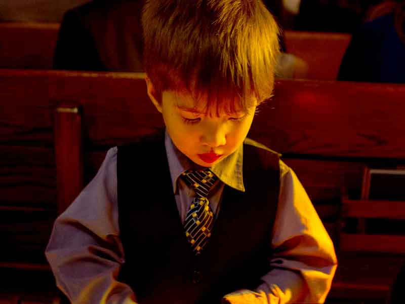 A young boy in a vest and tie sitting in church