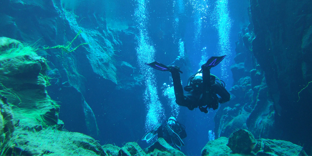 Scuba divers surrounded by bubbles and neon green algae - Diving Iceland's Silfra