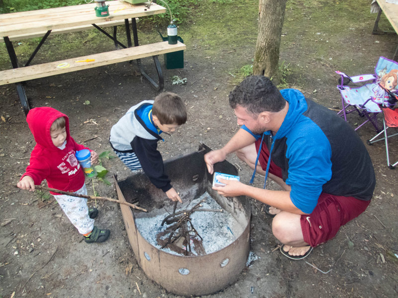 A father and two young boys work to light a fire while camping in Mara Provincial Park with kids