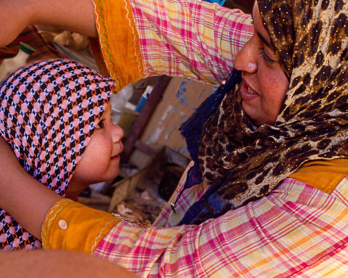 A young boy has a headscarf placed on him by a Bedouin woman