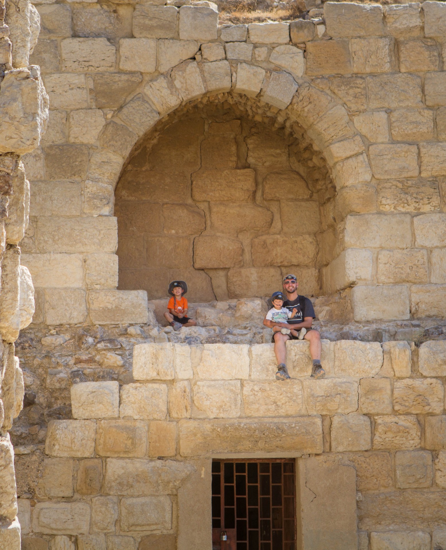 Father and two young boys sit on the walls of a castle