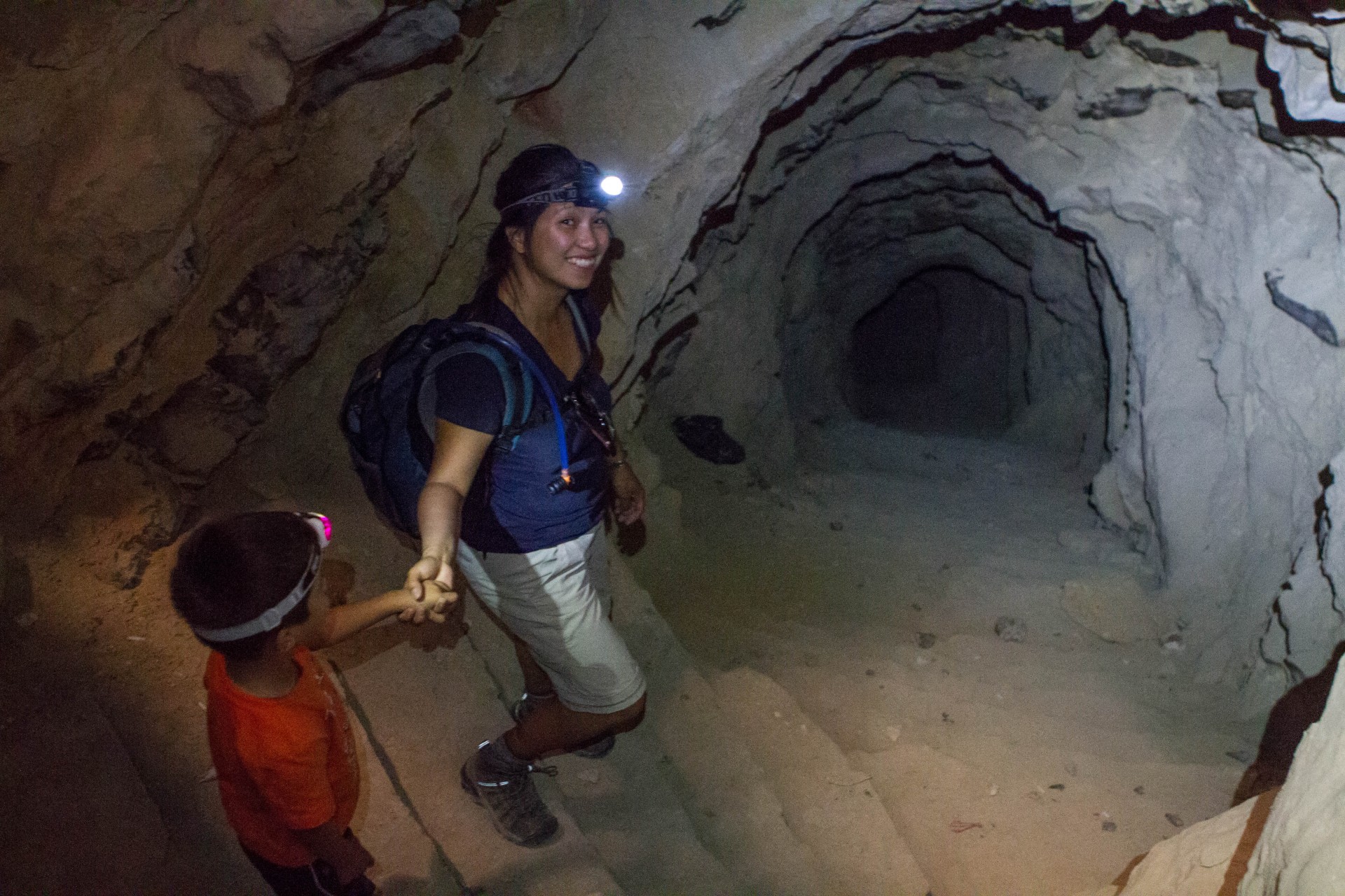 Woman and young boy with head lamps exploring a long tunnel
