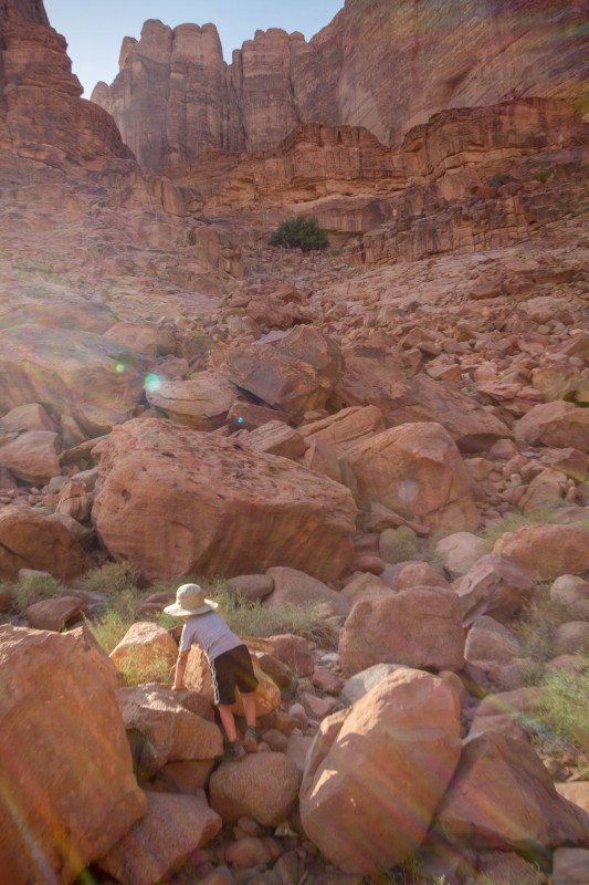 Young boy wearing a hat climbs over the red rocks of the Wadi Rum desert