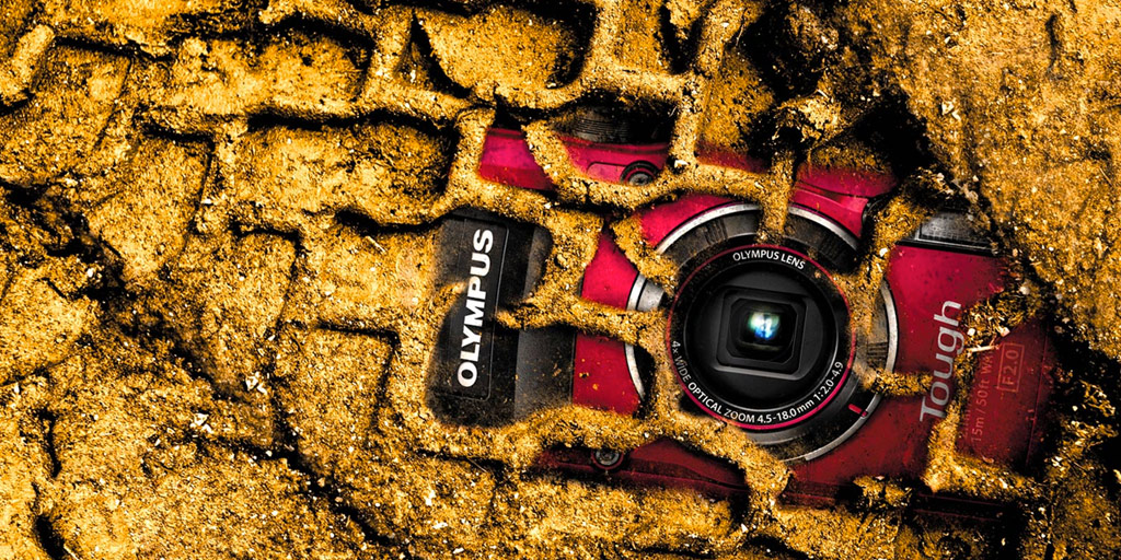 a red camera lies buried in dirt and tire tracks