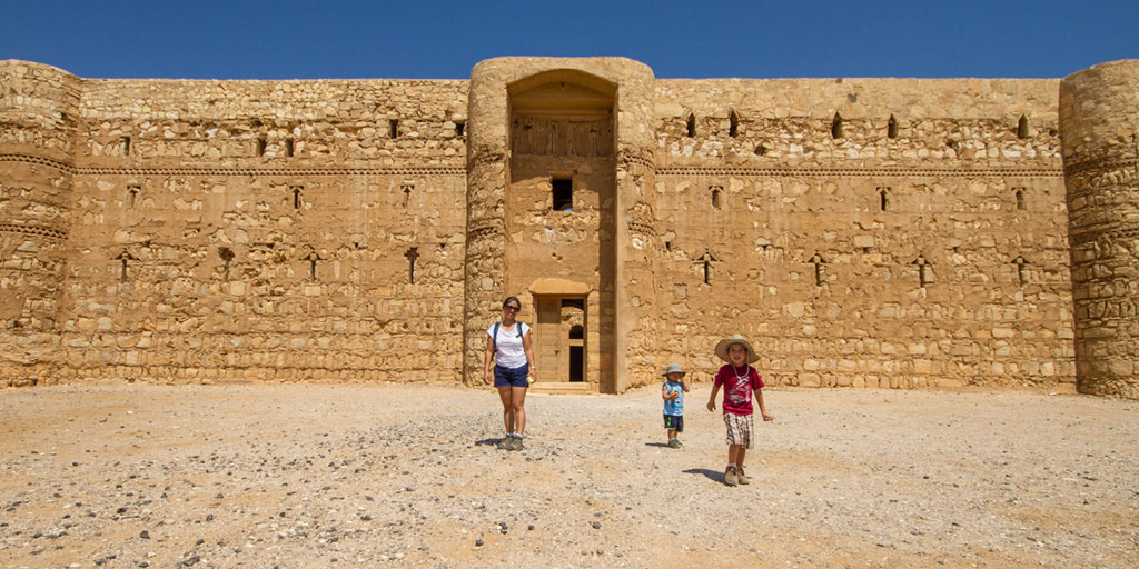 a woman and two young boys walk out of a large desert castle in Jordan