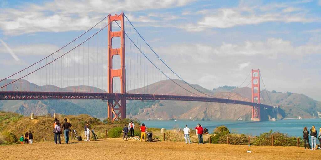 people walk along the coast below the Golden Gate Bridge in San Fancisco