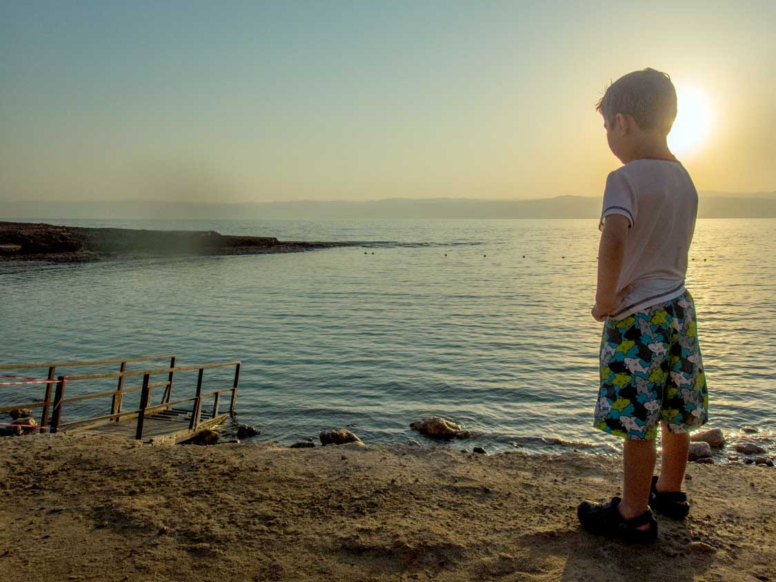 A boy, silhouetted by the sunset, looks out over the Dead Sea in Jordan
