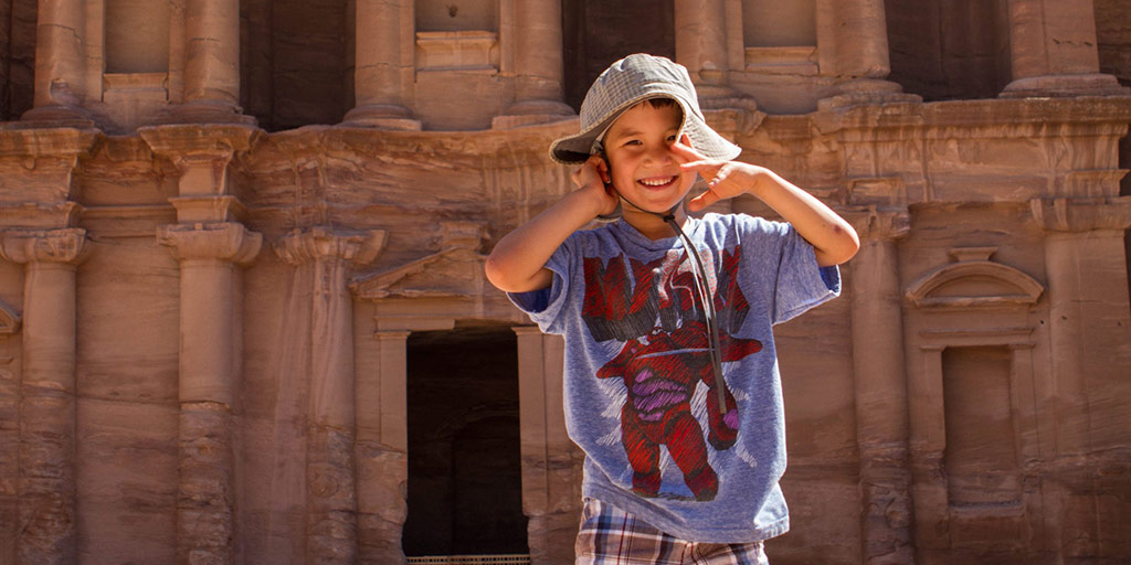 Young boy smiling and holding his hat in front of Petra's Monastery