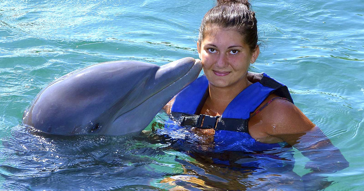 Woman in a life vest getting kissed by a dophin