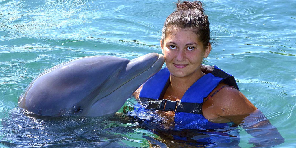 Woman in a life vest getting kissed by a dophin