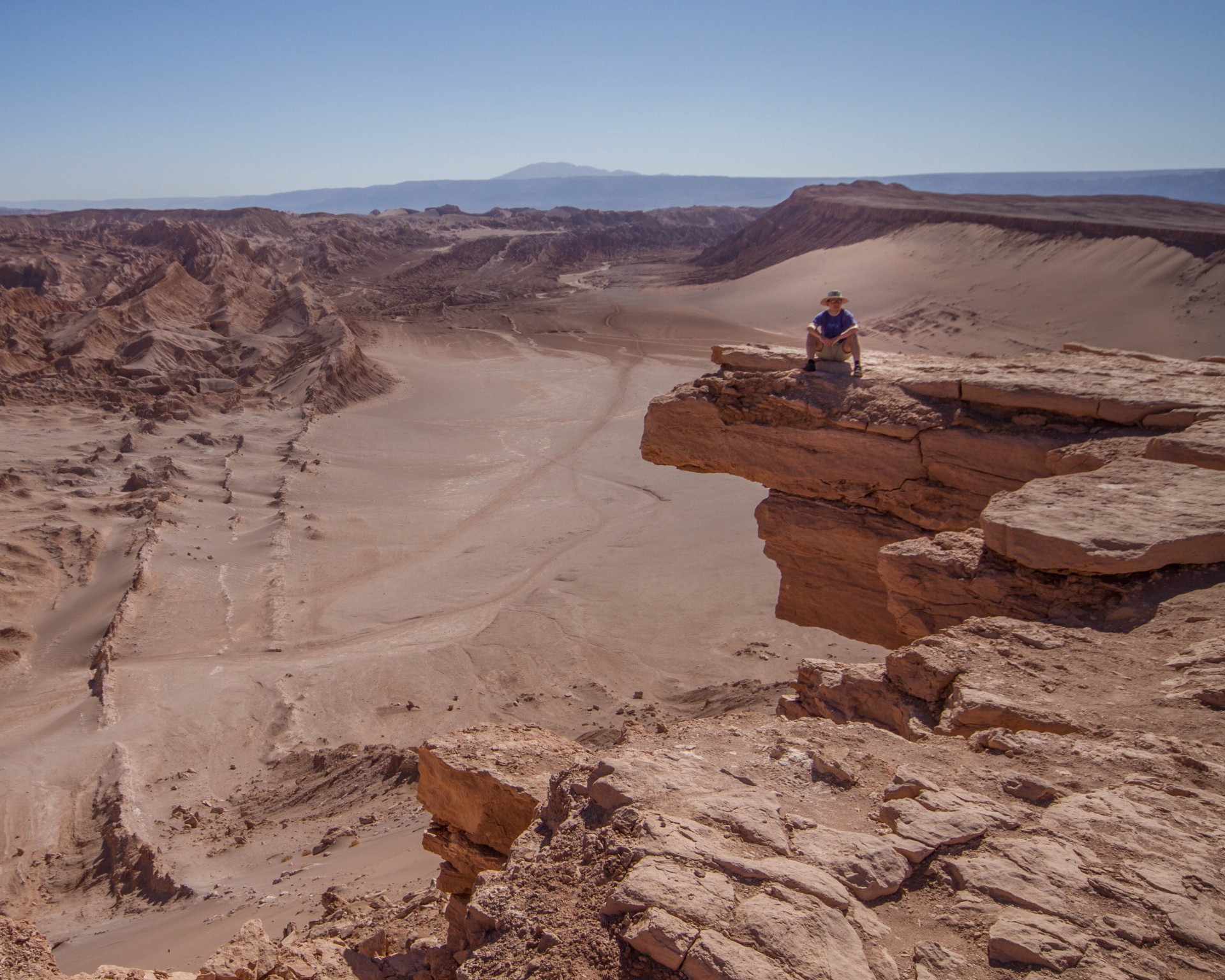 A man sits on a rock outcrop looking out over Valle de la Muerte in Chile