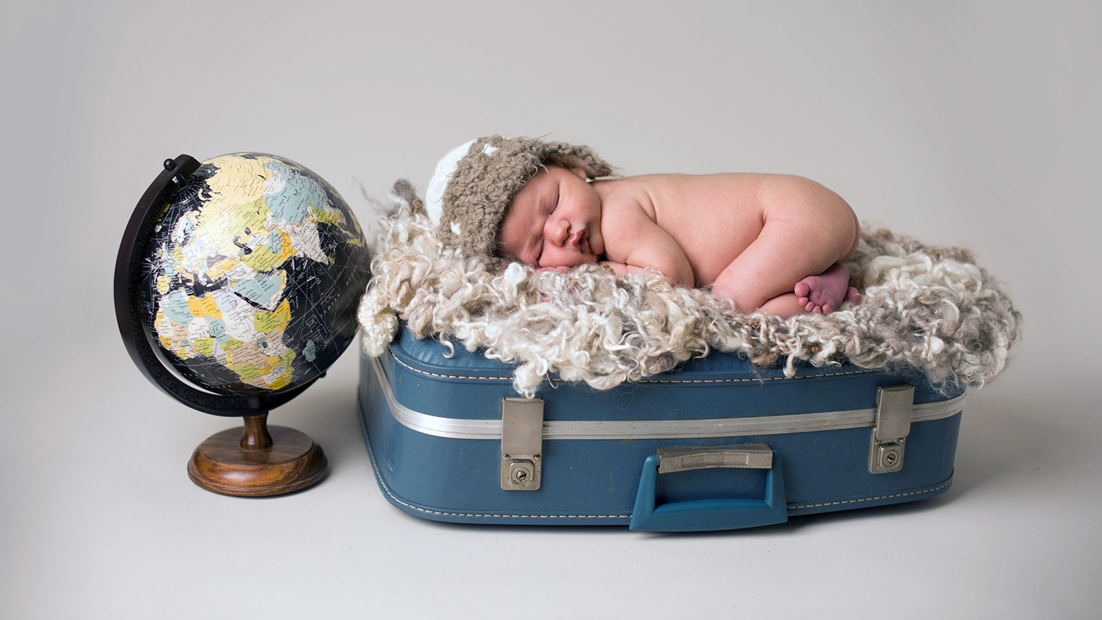 Baby sleeps on a piece of luggage next to a globe - helping kids find nap time on the road