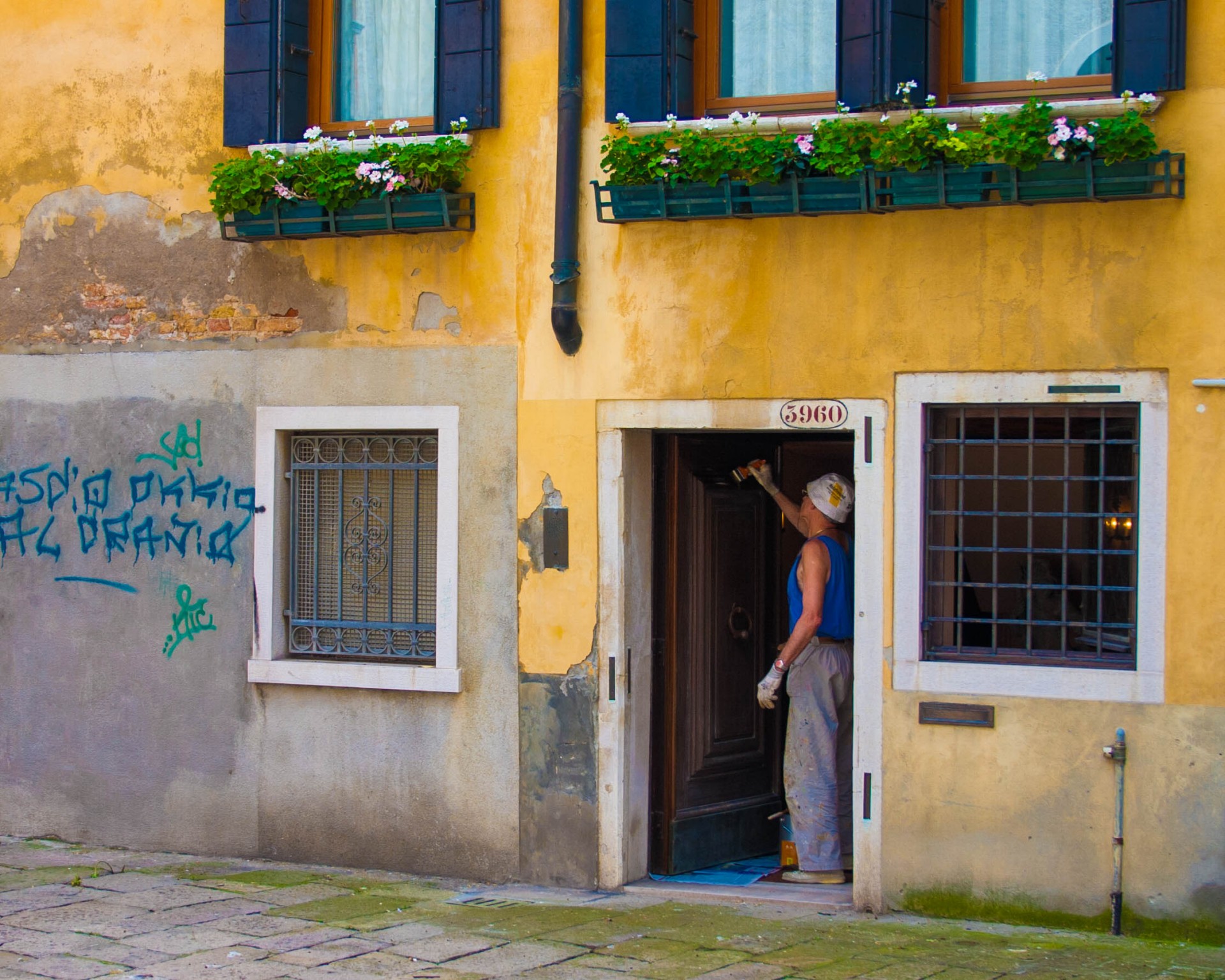 A man paints the white door frame of a yellow house in Venice, Italy - Lost in Venice