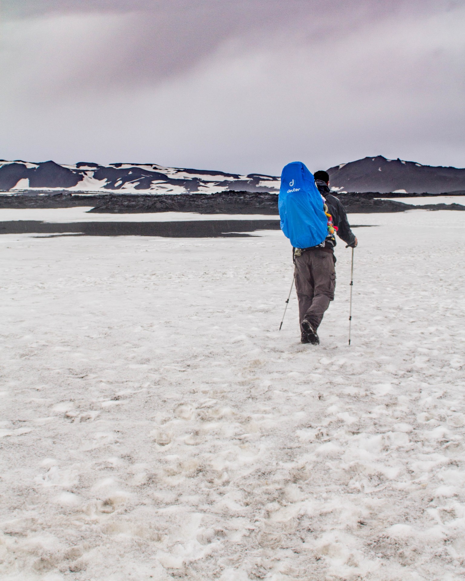 Man hiking through snow with a child in a kid in a Deuter Kid Comfort III Kid Carrier with a blue rain cover