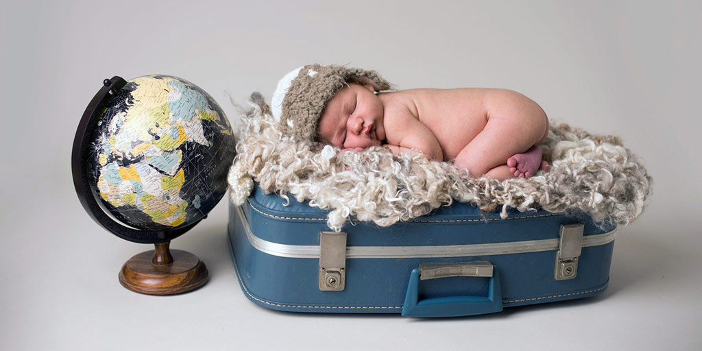 a little baby sleeping on a suitcase next to a globe