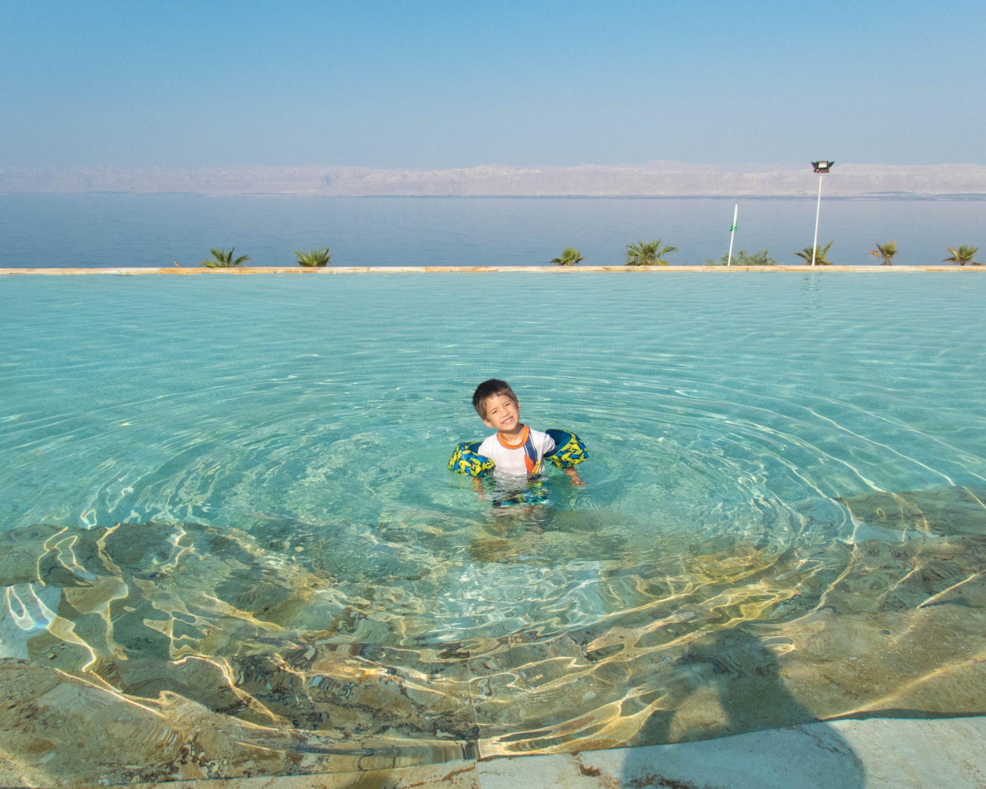 young boy smiles while in a pool with the Dead Sea in the background