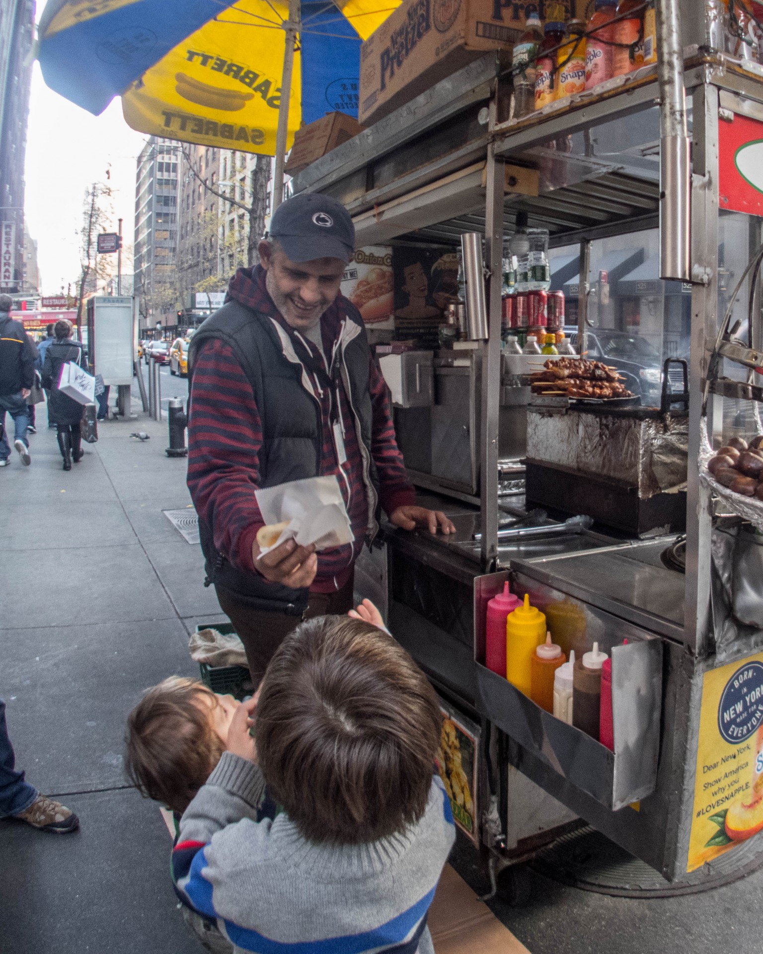 A smiling hot dog vendor hands the boys a warm pretzel on the streets of New York
