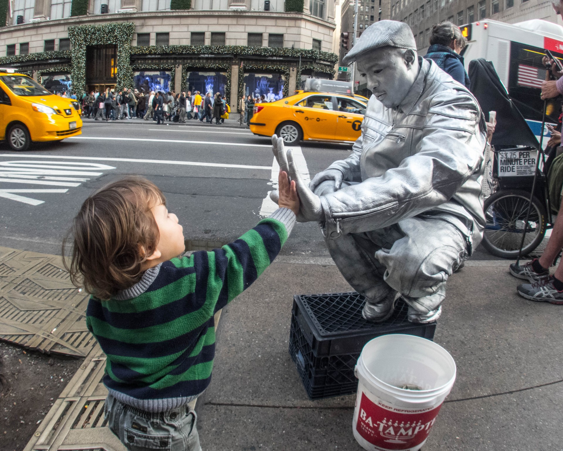 Young boy gives a high five to a street performer wearing silver body paint and a silver outfit