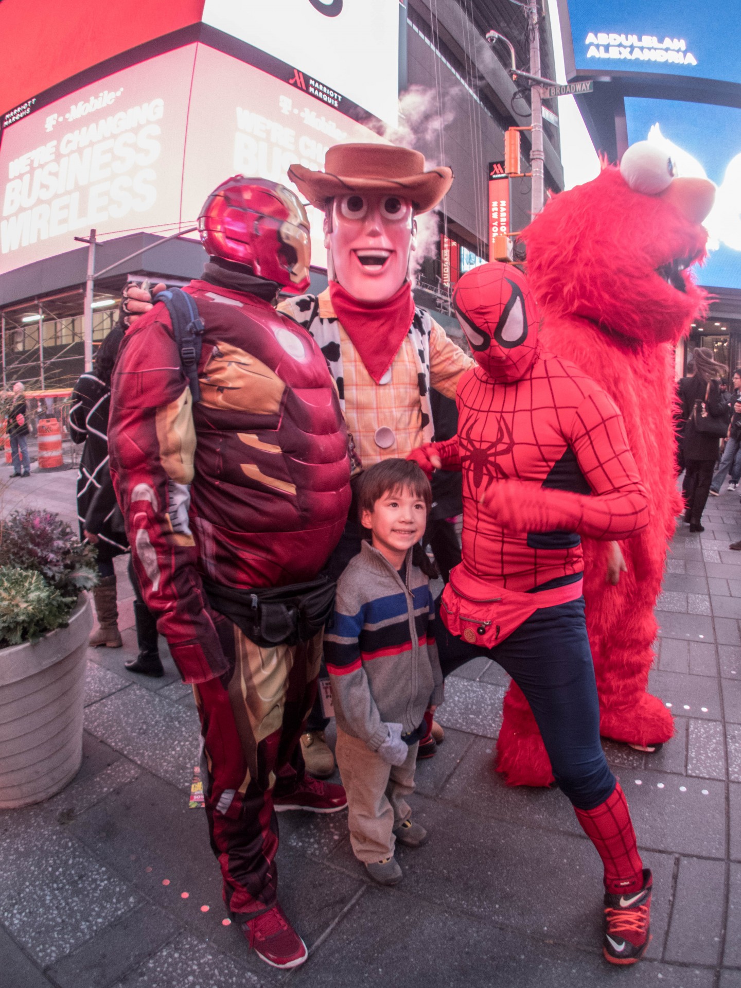 Young boy smiling next to street performers in Iron Man, Woody and Elmo costumes