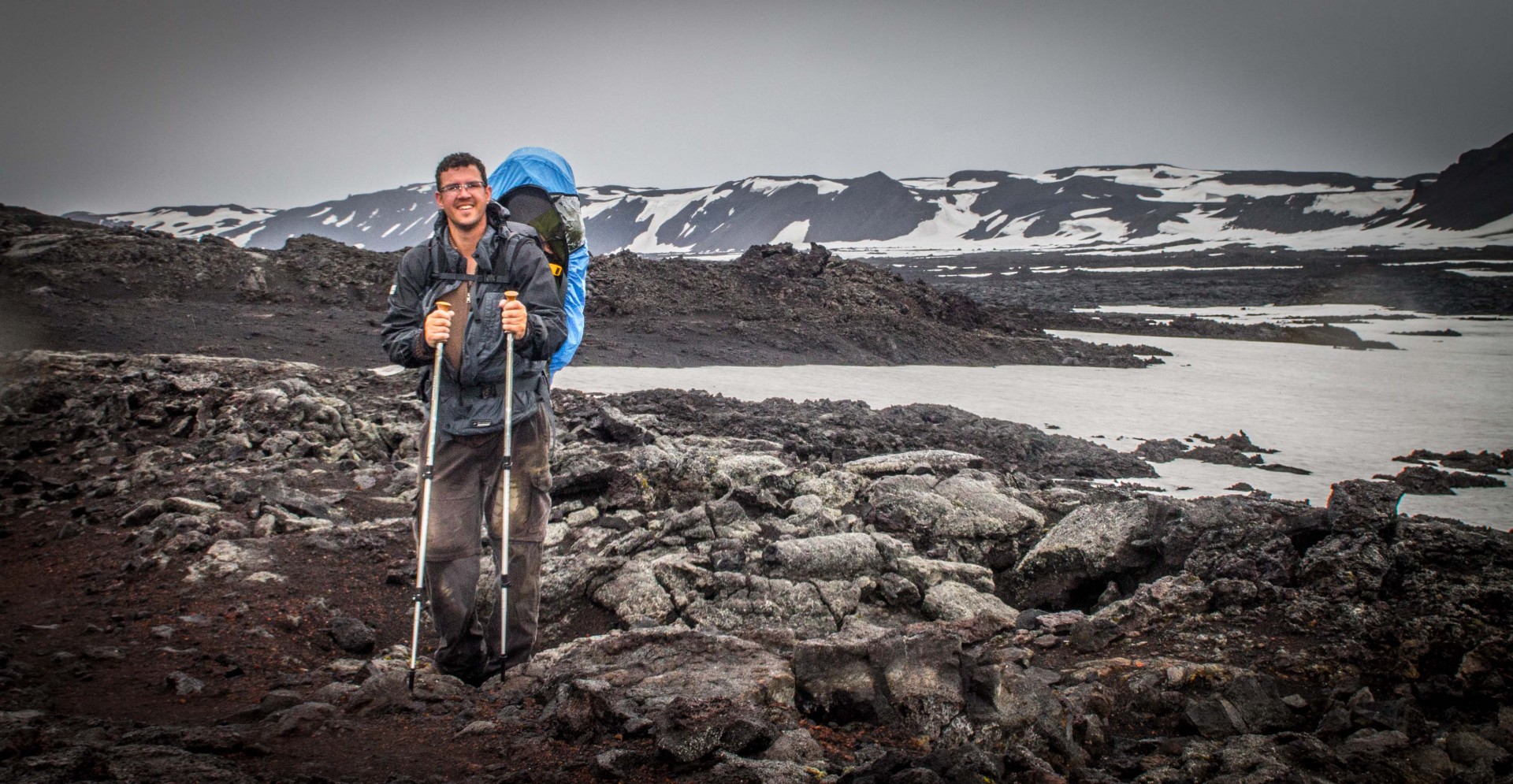 Man carrying infant in a kid-carrier standing on rocks and snow in the Icelandic Highlands