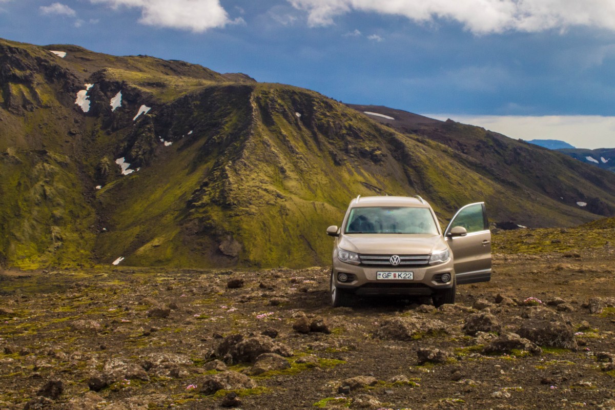 A volkswagen tiguan sits on rough ground with green hills in the background - Icelandic Highlands