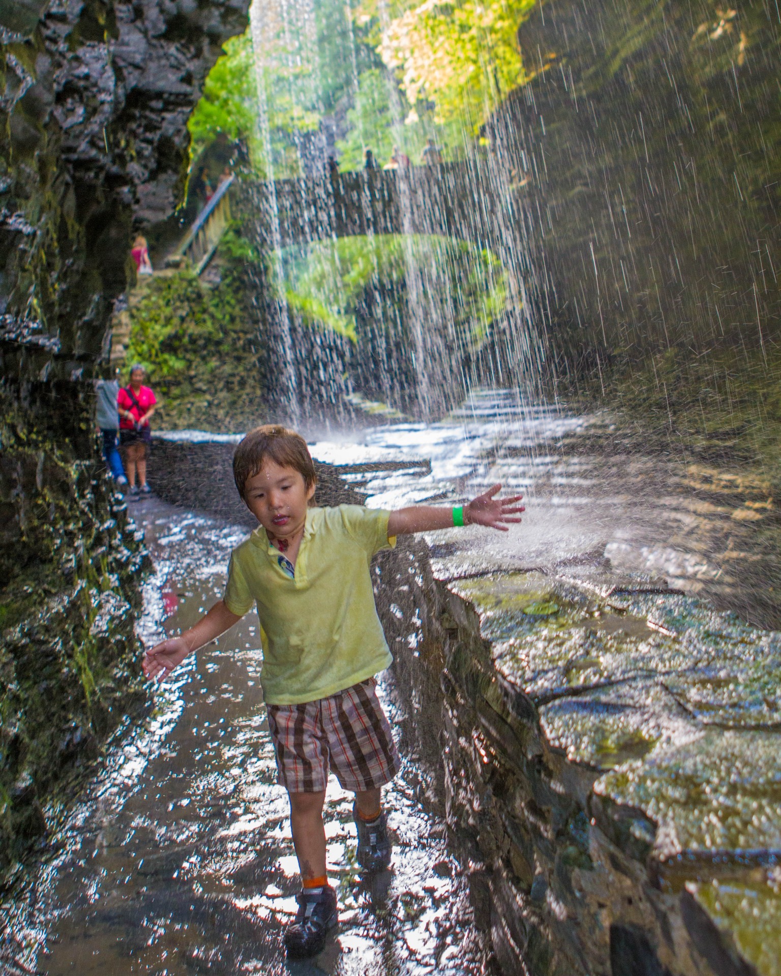 Boy playing under Rainbow Falls in Wakins Glen State Park.