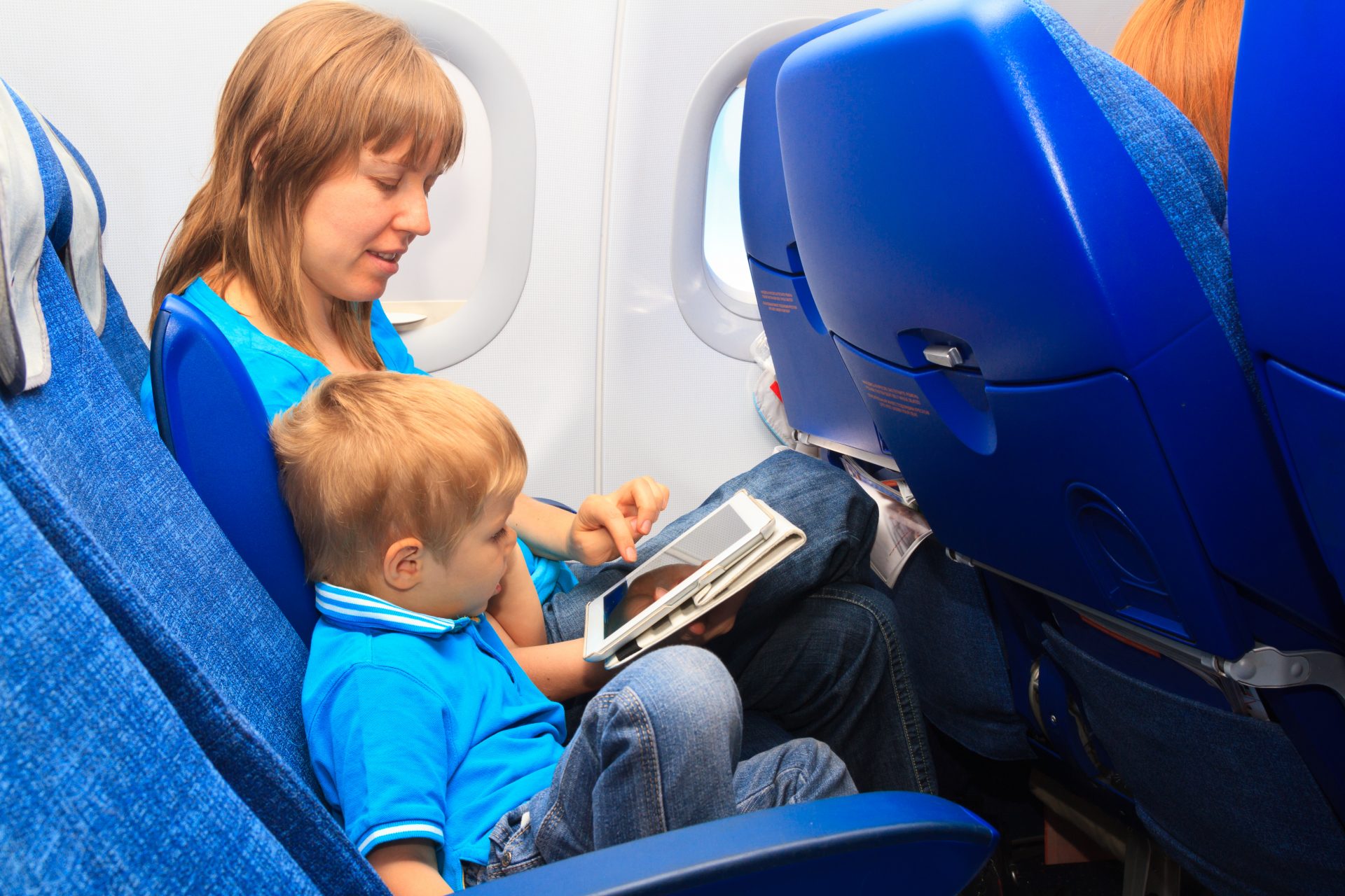 Mother plays games on a tablet with her young son as they fly on an airplane - - Flying with a baby