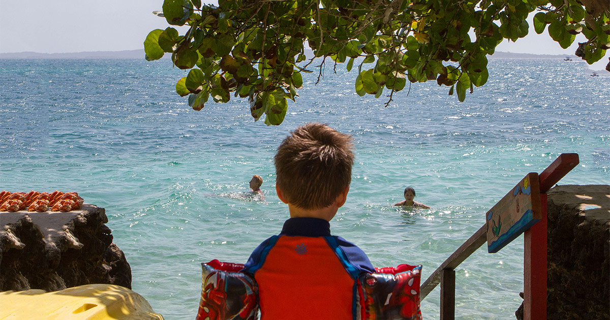 Young boy wearing water wings looking out over a tropical ocean