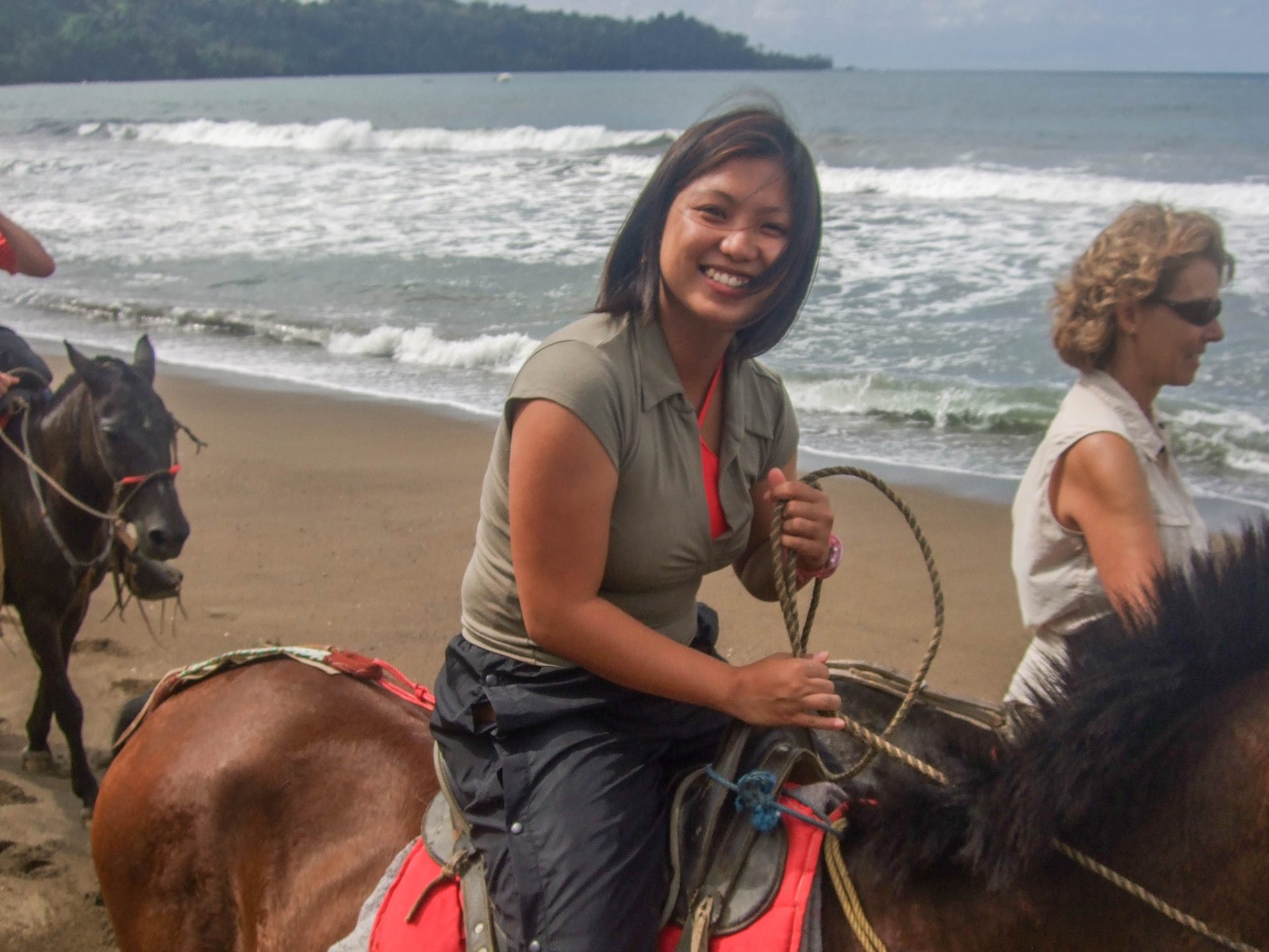 A young woman smiles at the camera as she rides a horse along the beach - finding paradise on the Osa Peninsula