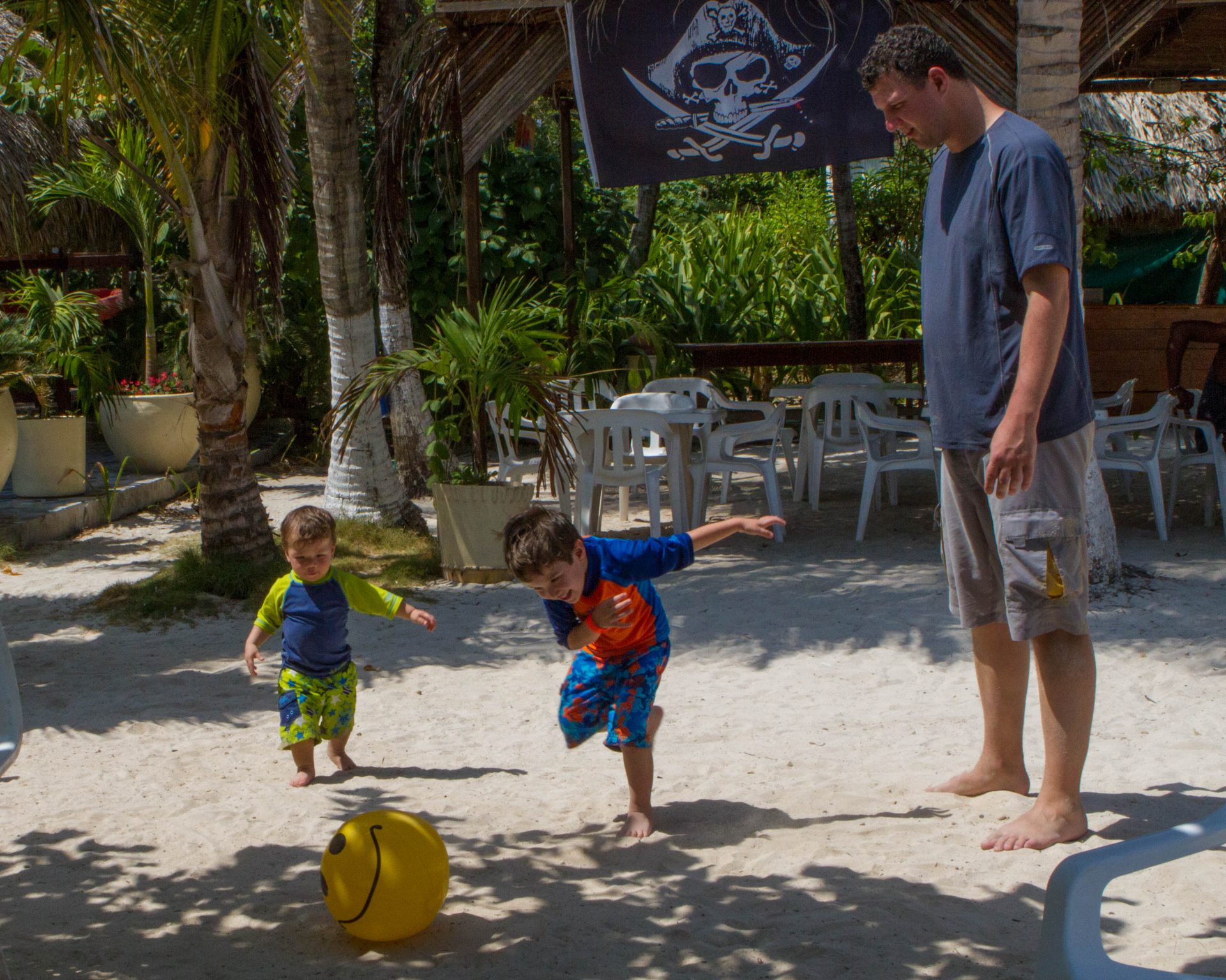 Boys playing soccer with a beach ball in the sands of Pirate Island while man watches.