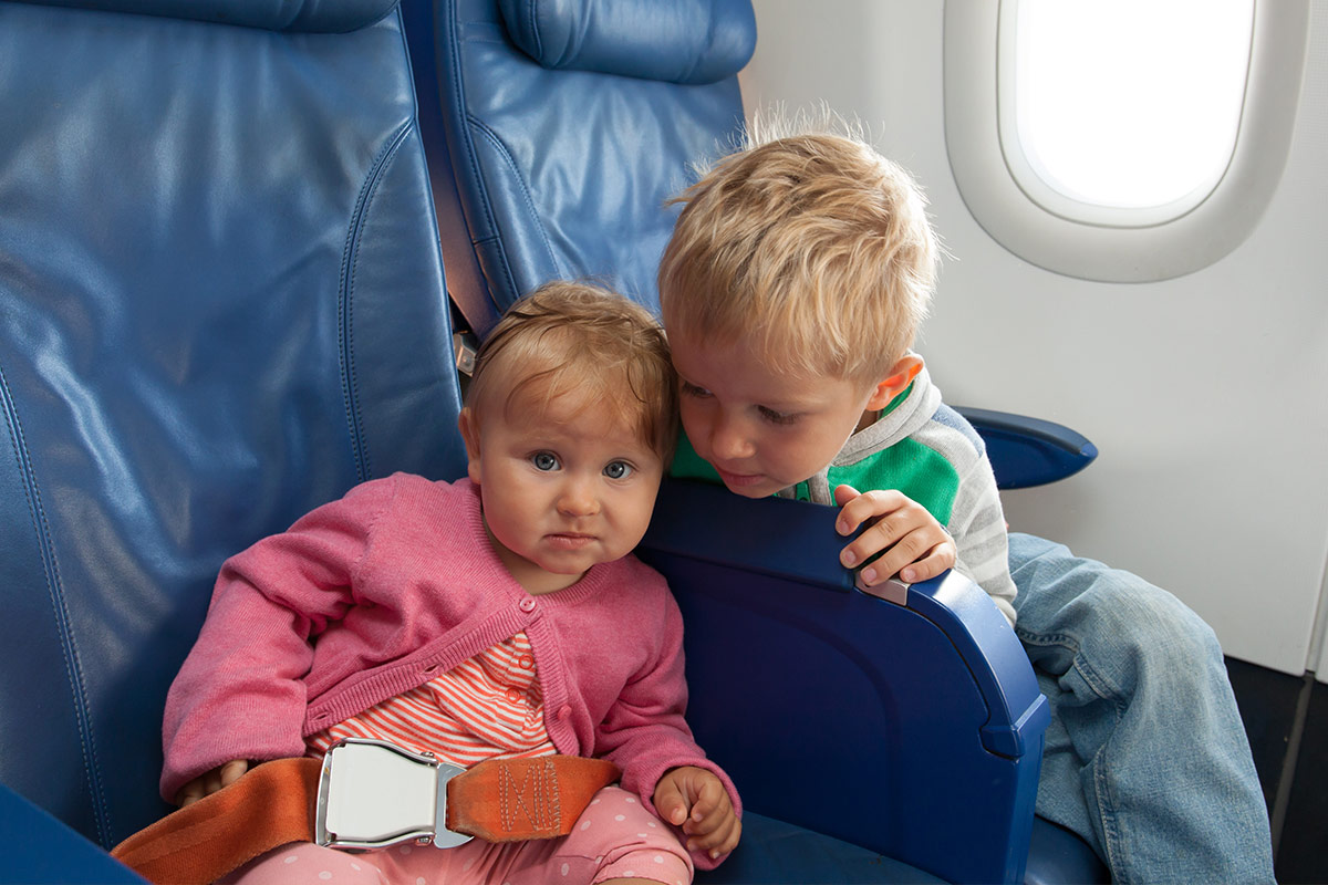 Young boy looks over an airline seat at his baby sister - Flying with a baby