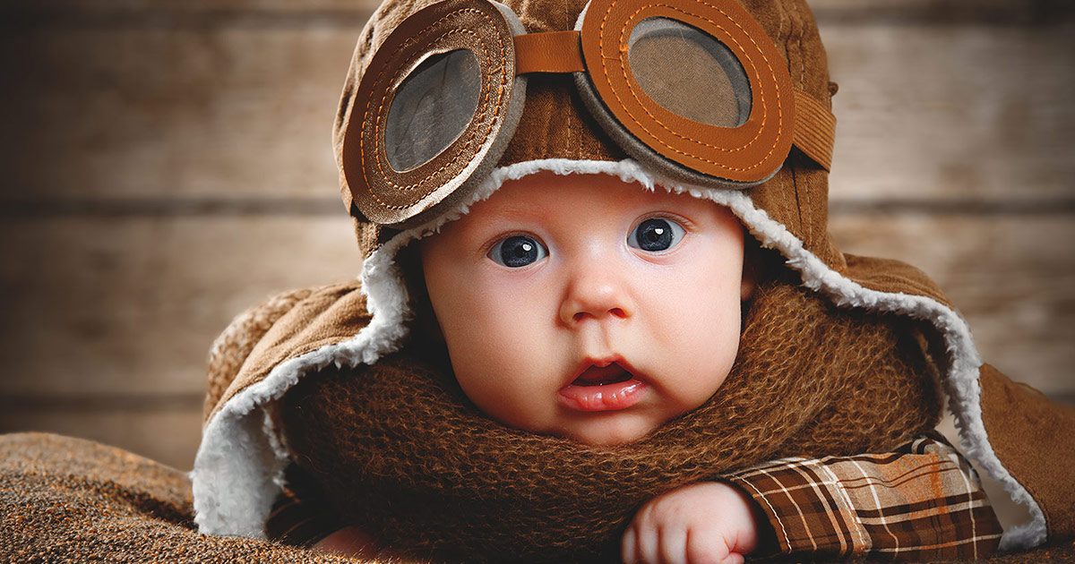 Baby in a vintage pilots outfit looking at the camera - Flying with a baby