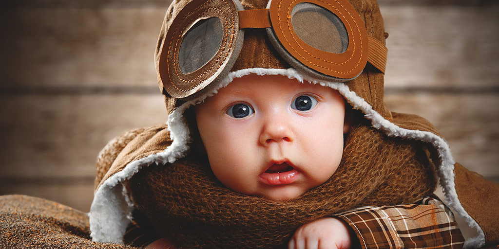 Baby in a vintage pilots outfit looking at the camera - Flying with a baby