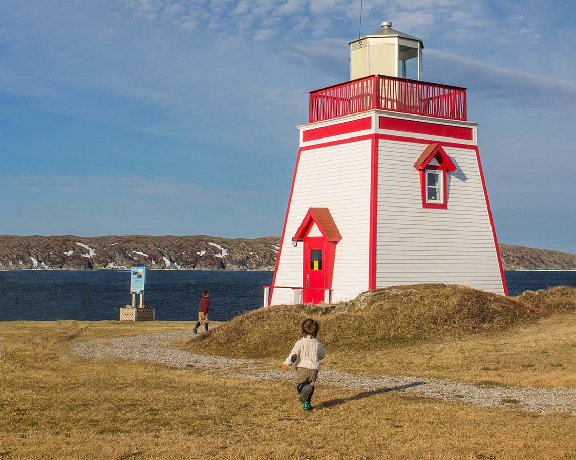 Children run toward Fox Point Lighthouse in St Anthony Newfoundland