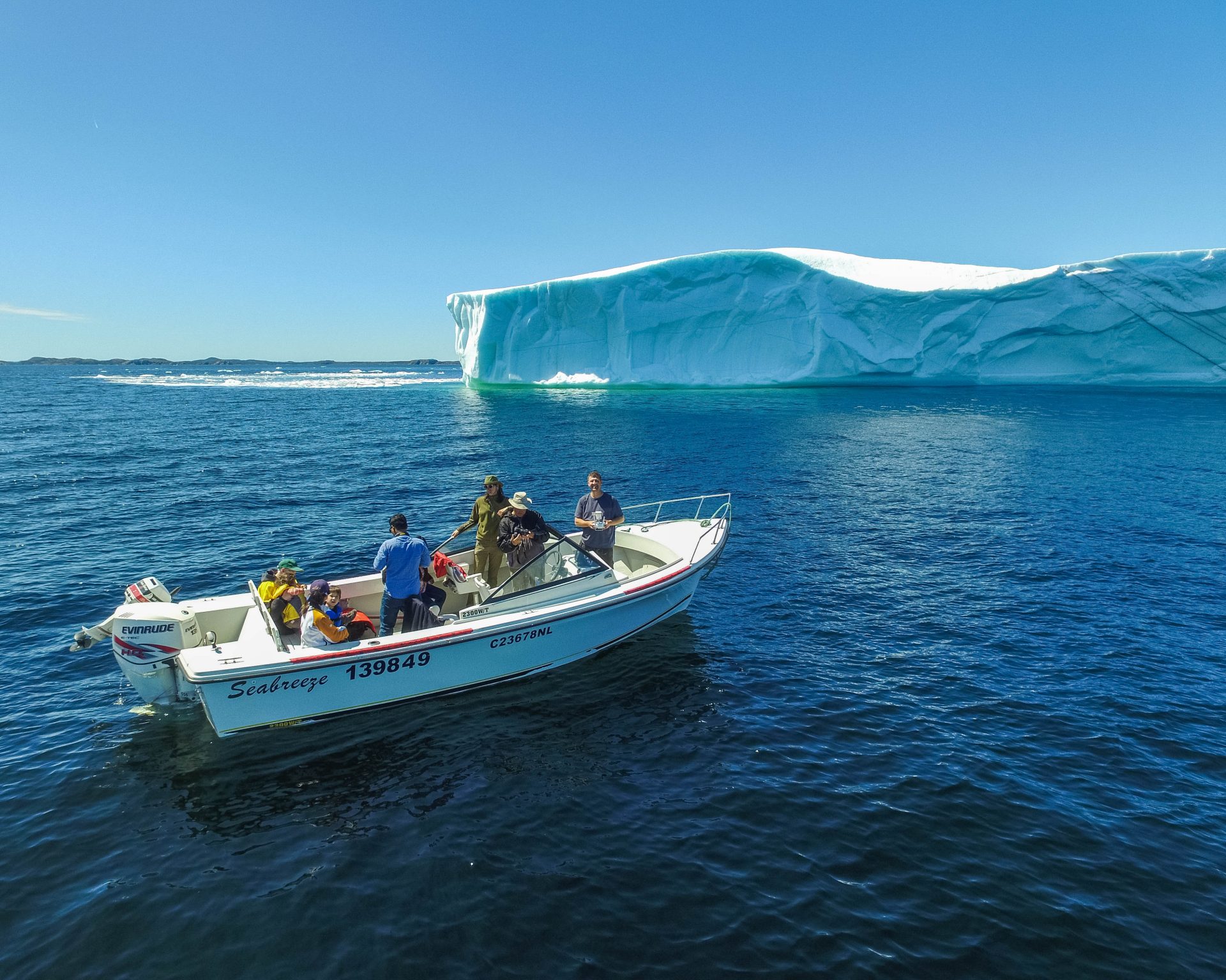 A small boat of tourists photographs a large iceberg in Twillingate, Newfoundland - Icebergs in Twillingate