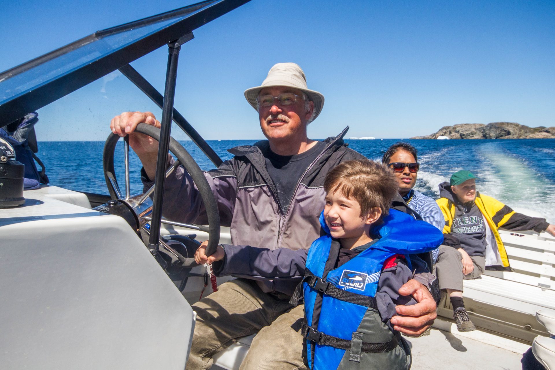 A man lets a young boy steer a motorboat as they ride on the ocean - Icebergs in Twillingate