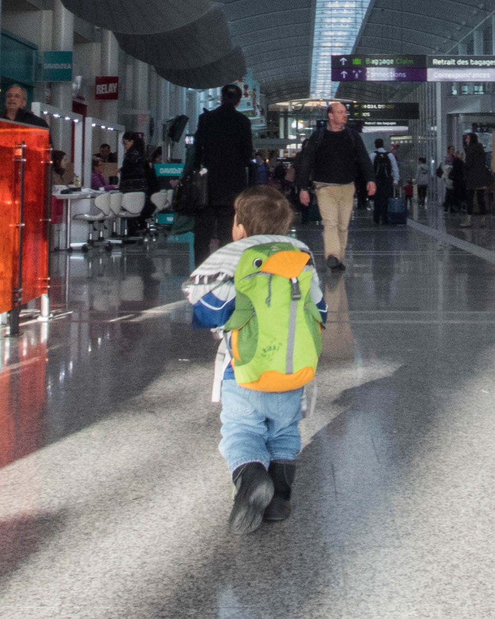 A toddler carrying a backpack walks through an airport