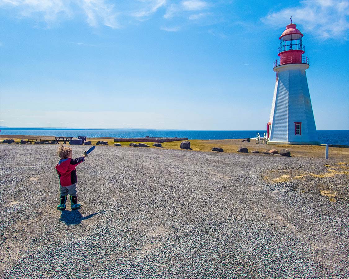 Young boy with a toy sword points at a Lighthouse in Newfoundland