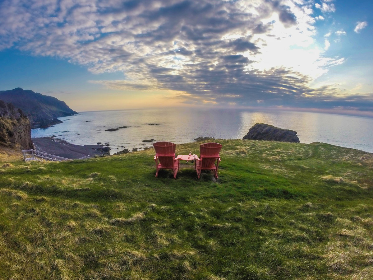 two red muskoka chairs sit on green grass on a cliff overlooking the ocean in Gros Morne National Park - Hiking Green Gardens in Gros Morne National Park