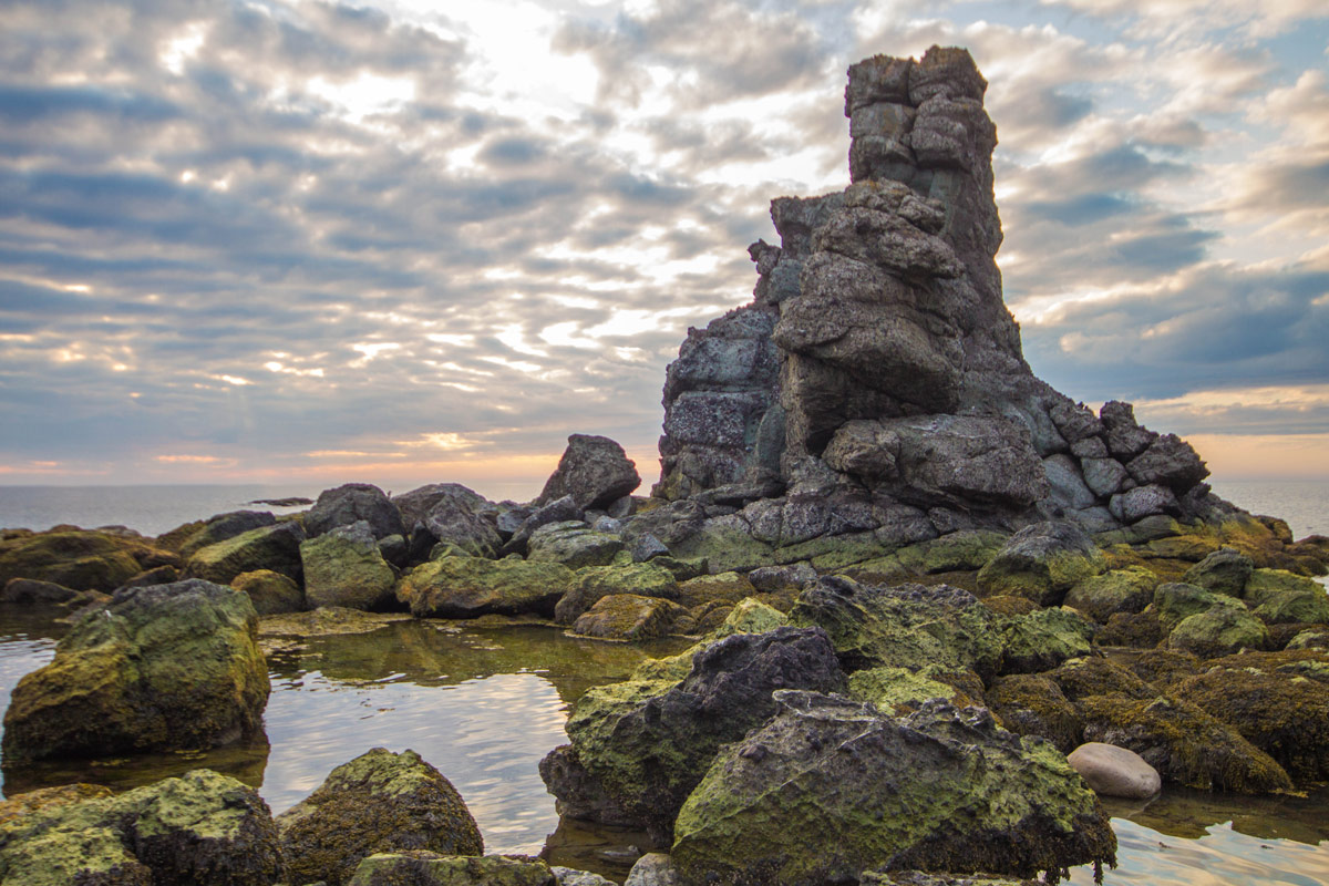 Volcanic stacks and rocks covered in green moss line the coast of Newfoundland with a spectacular sunset as a backdrop - Hiking Green Gardens in Gros Morne National Park