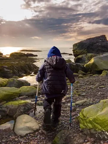 A young boy in outdoor wear hiking the Green Gardens Trail in Gros Morne National Park toward the ocean